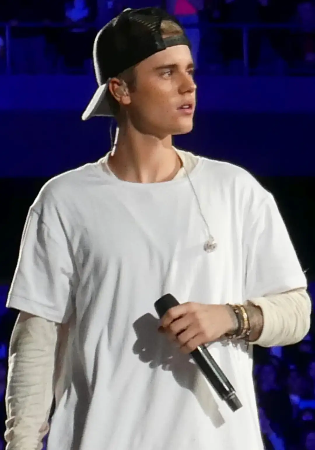 Justin Bieber performing on stage in a backwards baseball cap, the cap covering his forehead so that no hairline is visible.