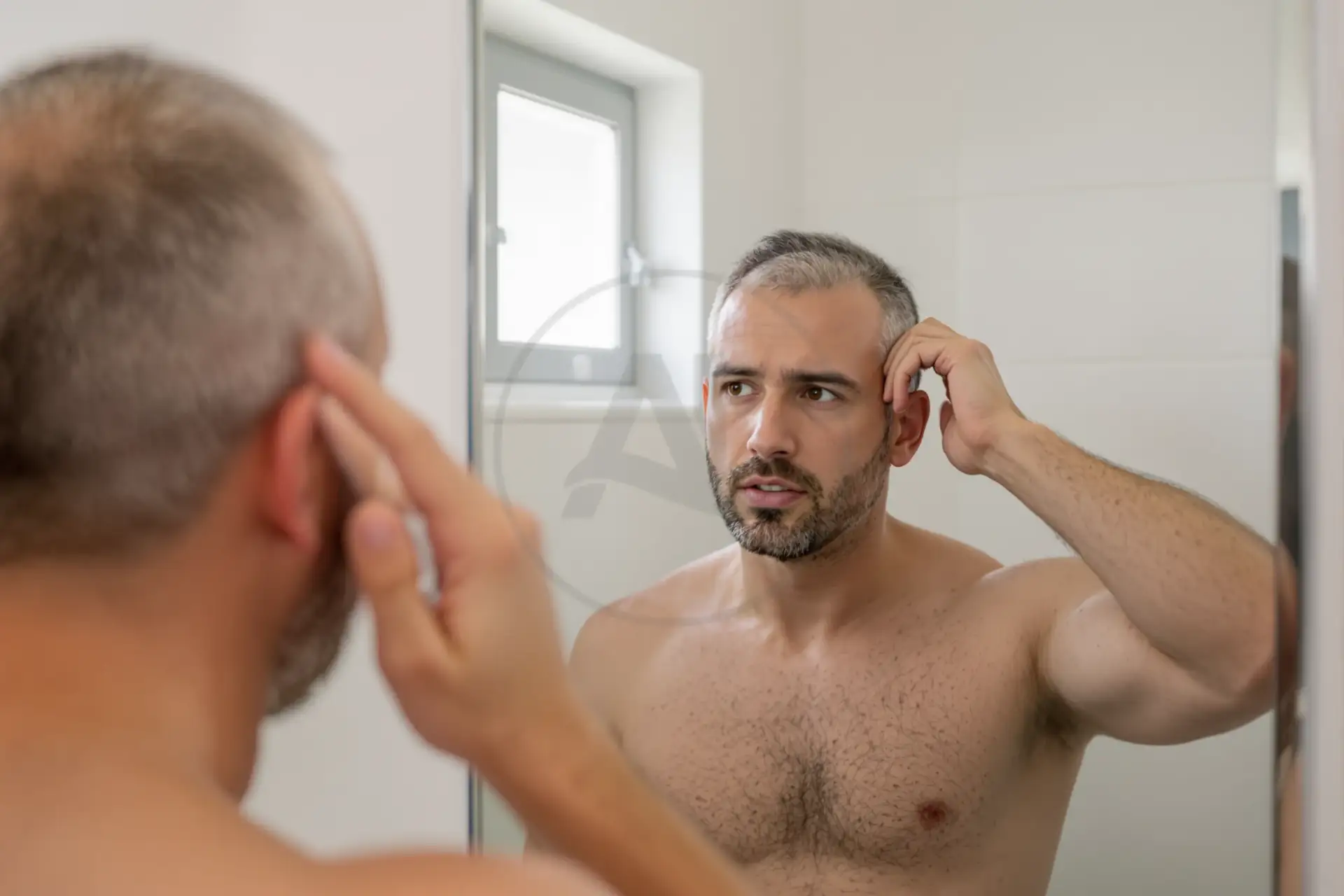 Uomo con capelli diradati si guarda allo specchio in bagno.