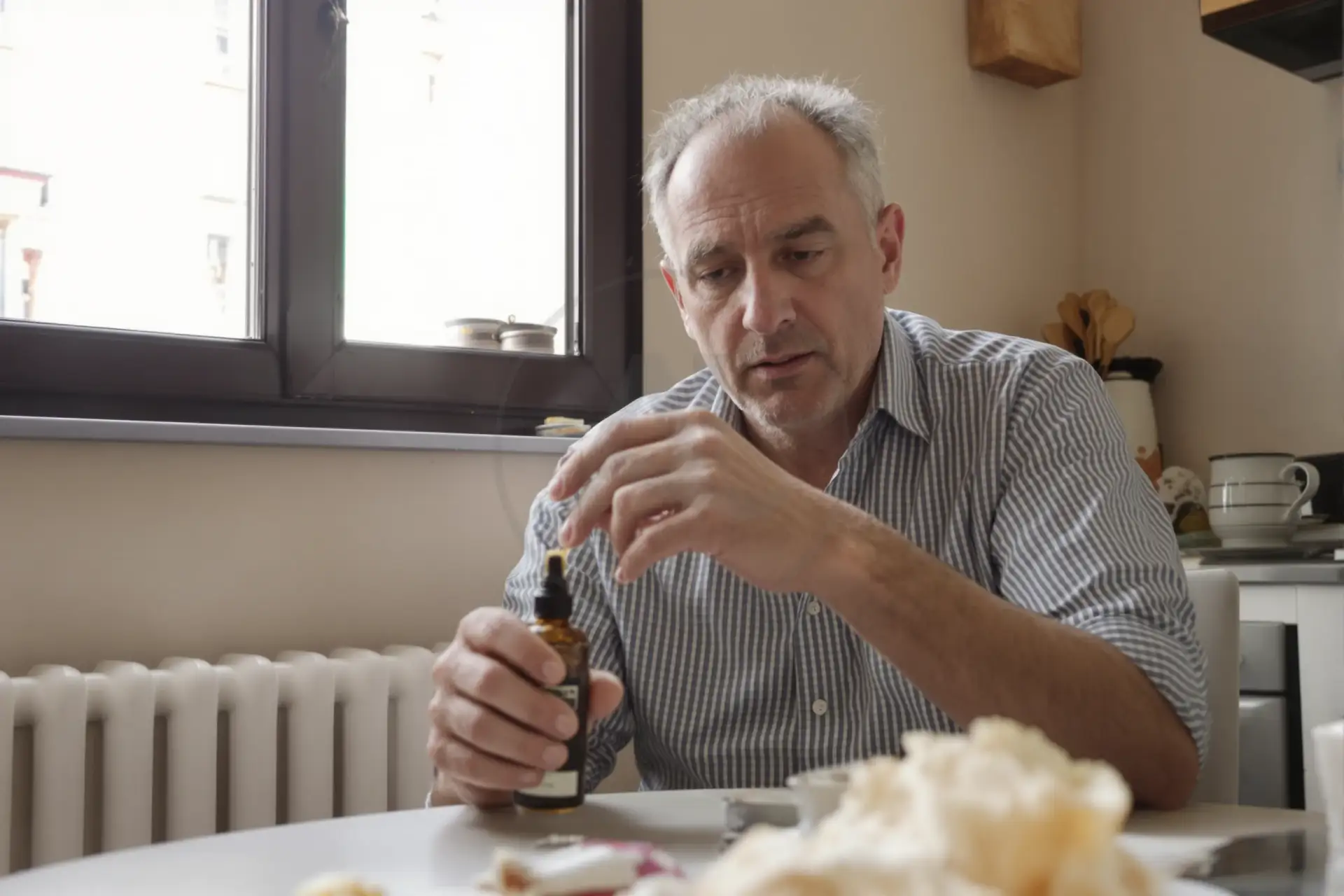 Older man at a kitchen table holding a dropper bottle of serum