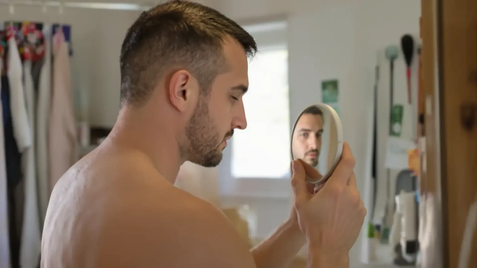 Man inspecting a thinning crown with a hand mirror in a bathroom
