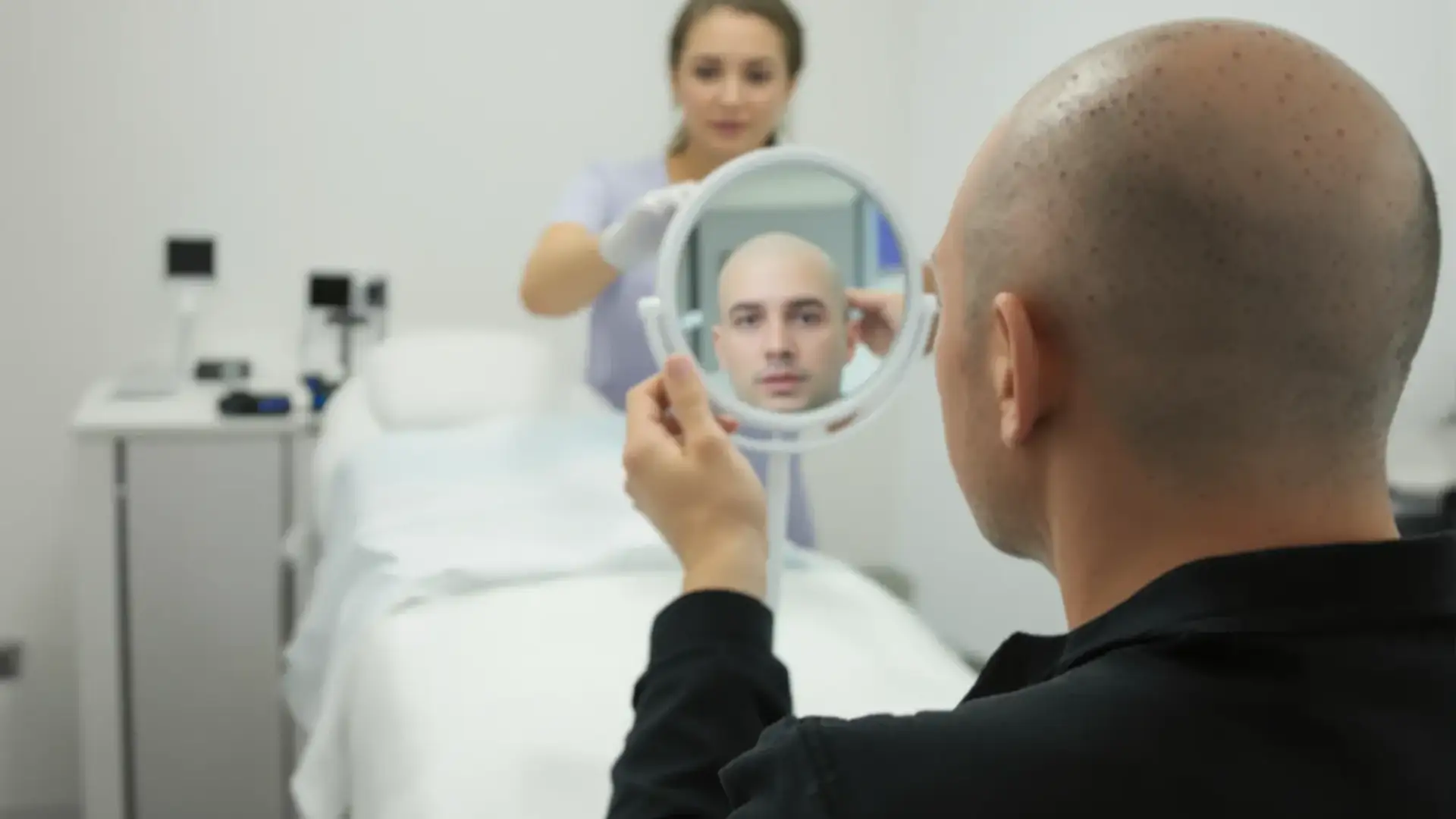 Man with shaved scalp and red grafts in a hair clinic, touching his head.