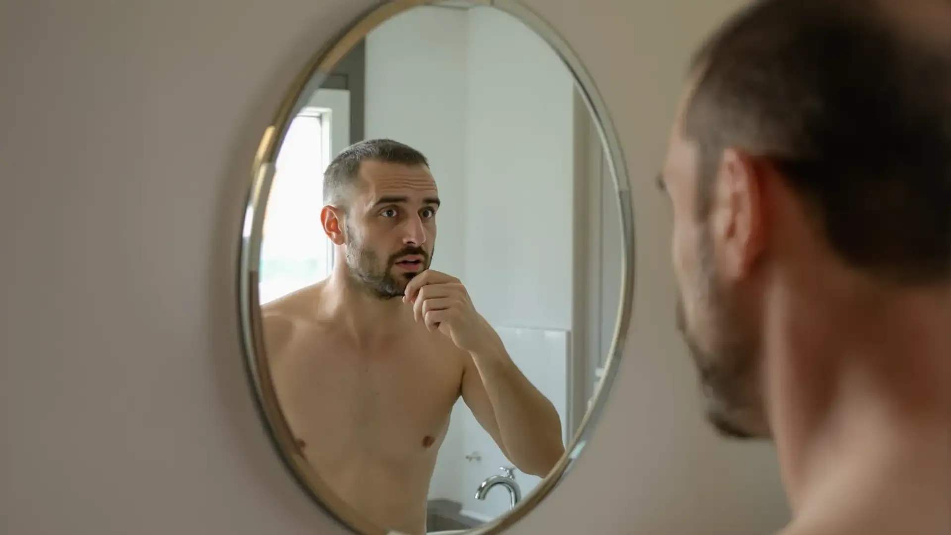 Uomo con capelli diradati si guarda l'attaccatura allo specchio in bagno