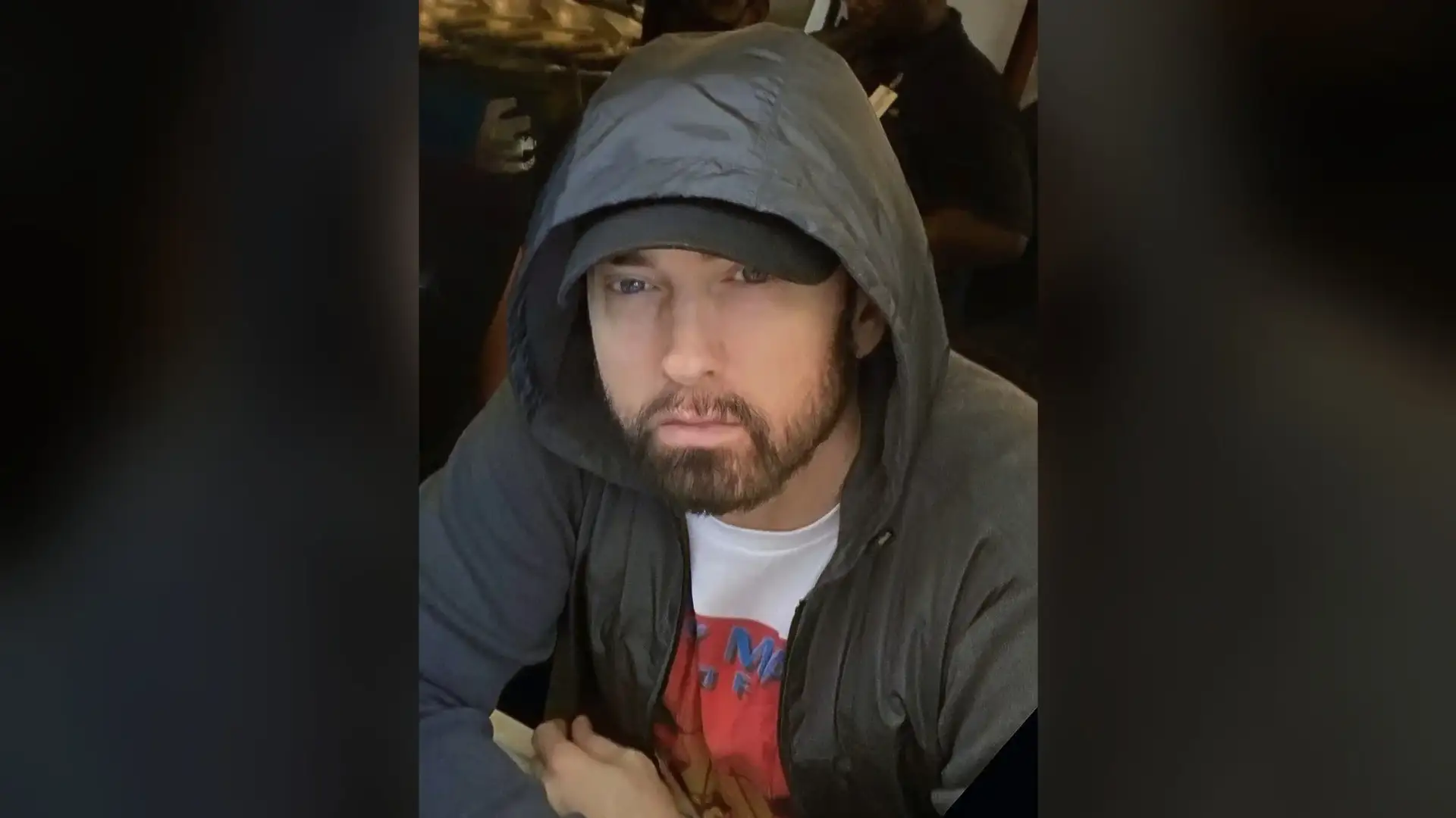 Eminem photographed indoors wearing a grey hooded jacket, his full beard and moustache clearly visible.