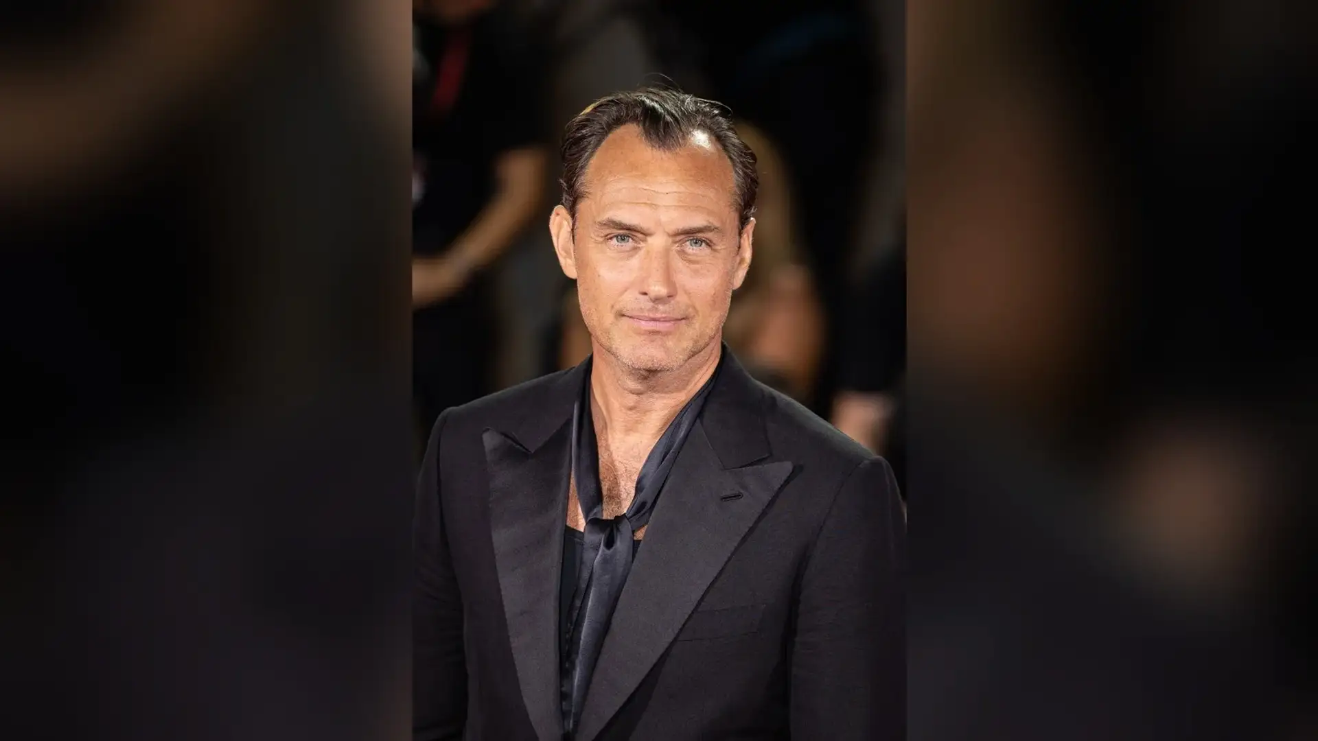 Jude Law in a black tuxedo on a red carpet, photographed from the front with his hair combed back and his front hairline in view.