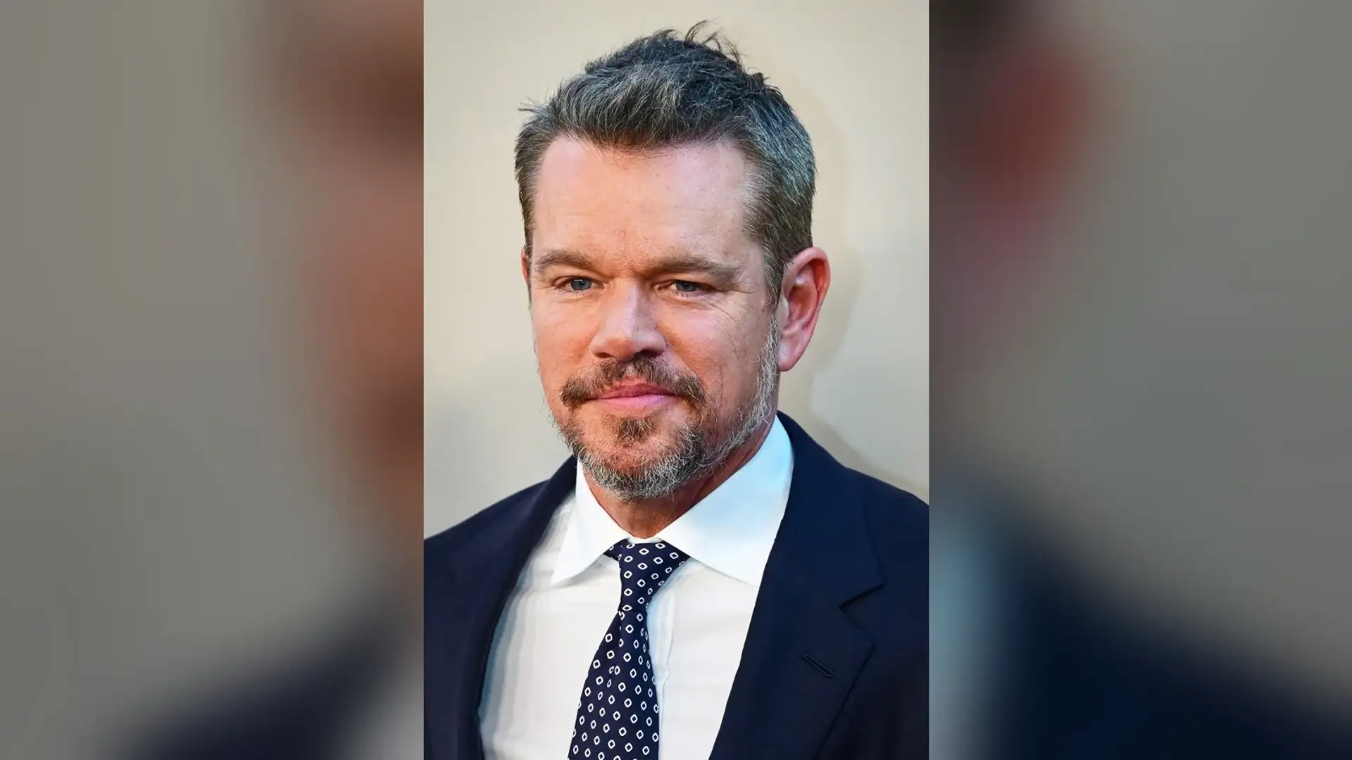 Matt Damon in a navy suit and patterned tie at a film premiere, seen from the front with his greying hair and hairline in view.