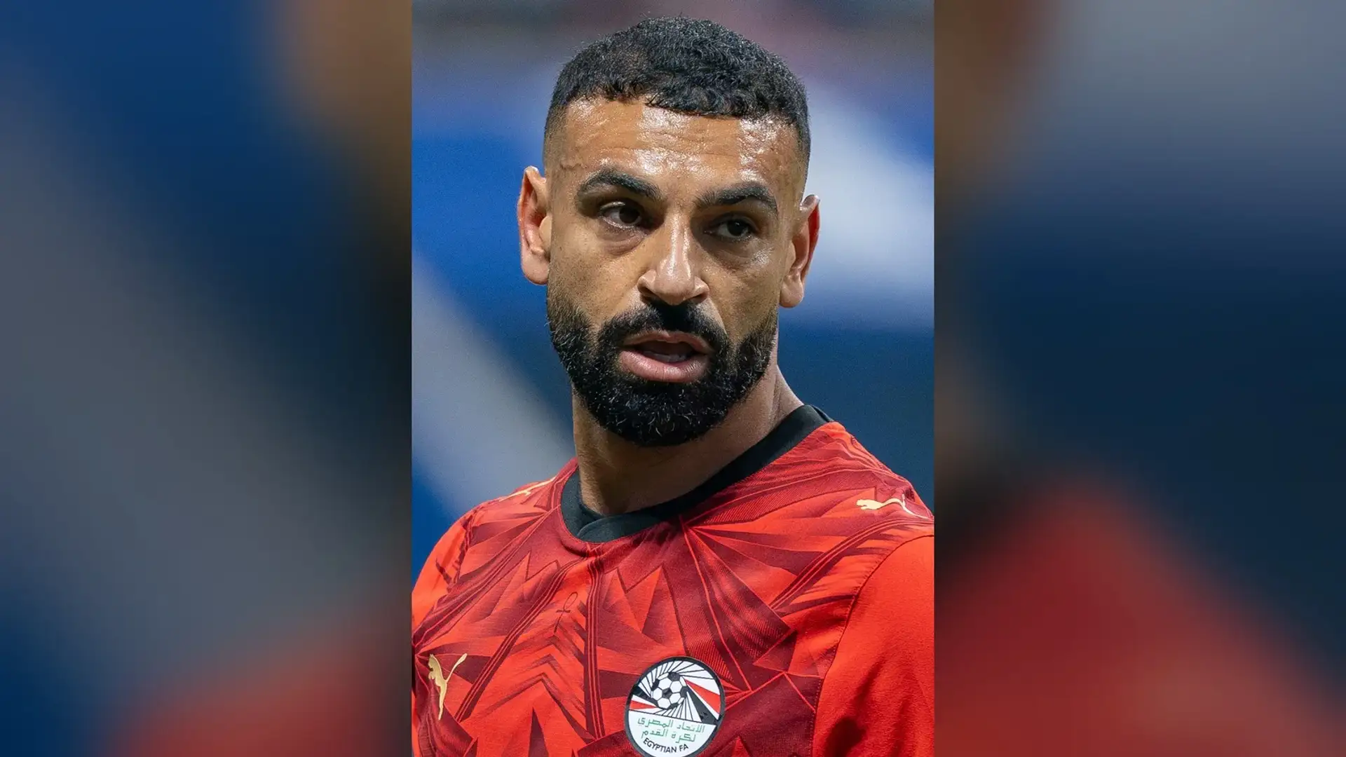 Mohamed Salah in a red Egypt national-team shirt on the pitch, seen head-on with his curly hair and temples visible.