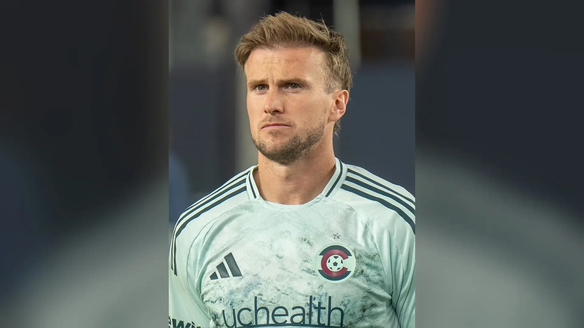 Rob Holding in a pale football kit photographed head-on before a match, his swept-back hair and hairline in view.