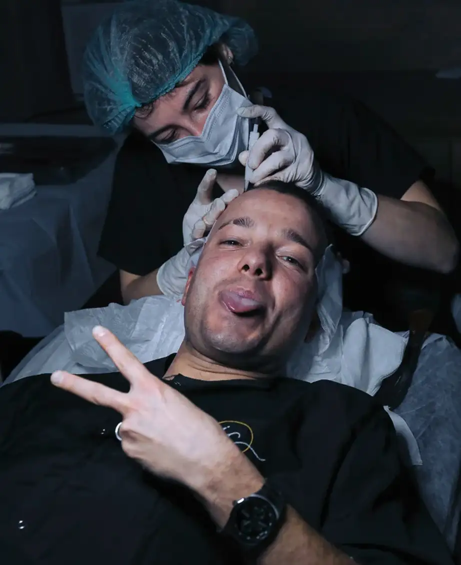Two clinicians in caps and masks working over an unidentified patient reclined in a treatment chair during a session.